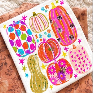 May include: A white fabric square featuring a colourful graphic print of six pumpkins in various shapes and sizes. The pumpkins are decorated with patterns including polka dots, stripes, hearts, and flowers, accented by small yellow and pink stars.