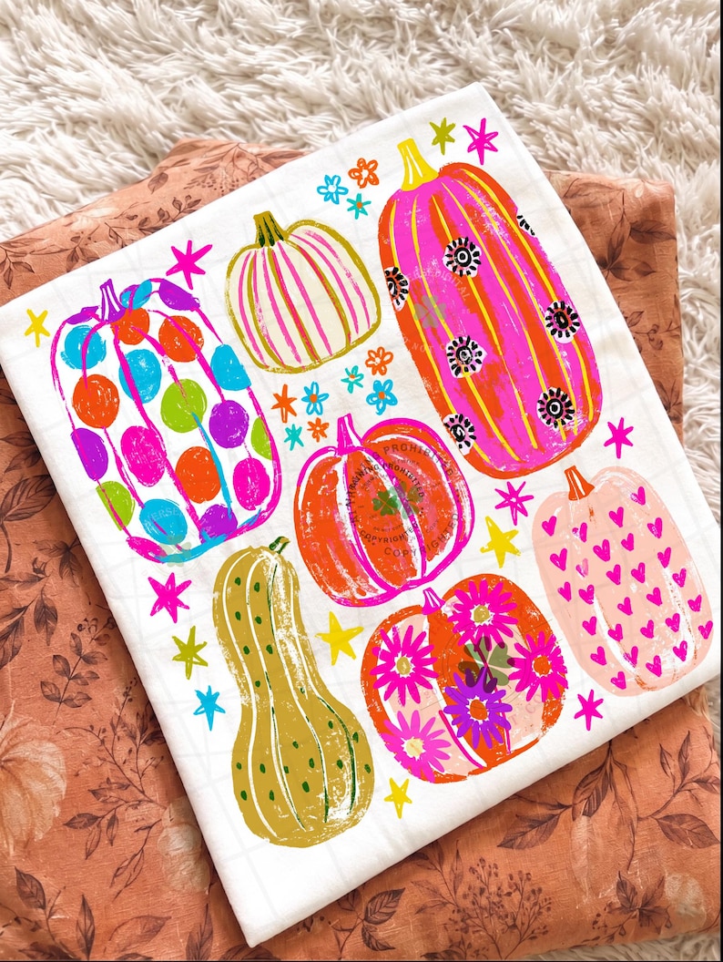 May include: A white fabric square featuring a colourful graphic print of six pumpkins in various shapes and sizes. The pumpkins are decorated with patterns including polka dots, stripes, hearts, and flowers, accented by small yellow and pink stars.