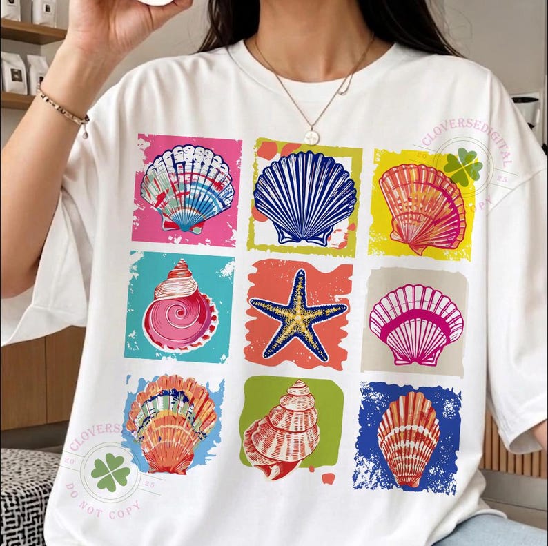May include: White t-shirt featuring a colorful graphic of nine seashells and a starfish in various colors and designs. The design includes pink, blue, orange, and yellow hues, with a distressed, textured background. The shirt has the text "CLOVERSEDIGITAL" and a four-leaf clover.