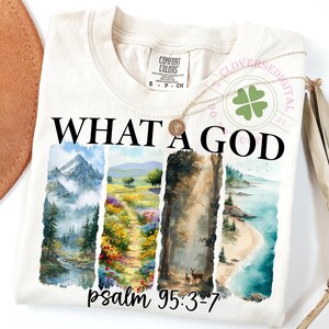 Può includere: T-shirt color crema con la scritta nera "WHAT A GOD". Sotto, un disegno di paesaggio ad acquerello con montagne, un sentiero e una scena di spiaggia. Il testo "psalm 95:3-7" è in basso.