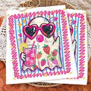 May include: A white t-shirt featuring a colorful graphic of a ghost wearing heart-shaped sunglasses, holding a glass of pink lemonade with a lemon slice, and surrounded by strawberries, all framed by a bright pink scribbled border on blue stripes.