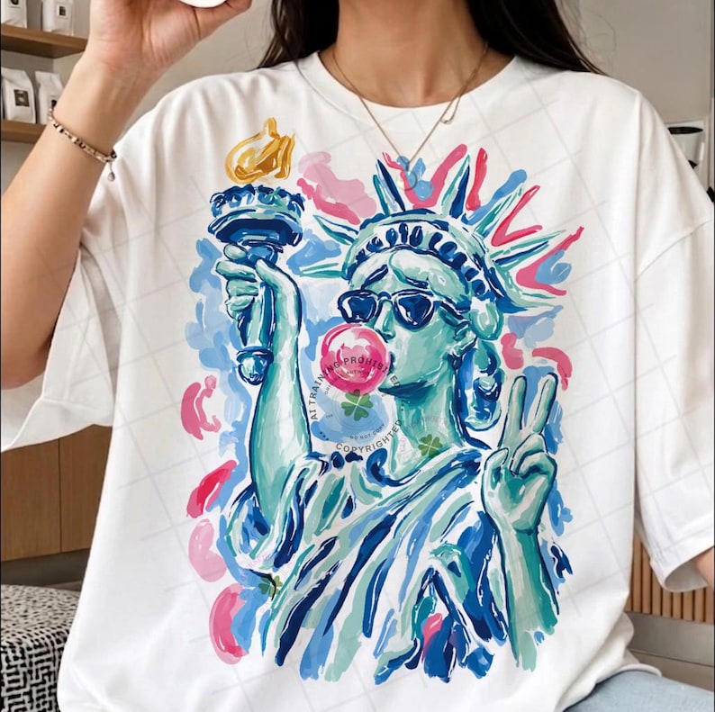May include: White t-shirt featuring a colorful illustration of the Statue of Liberty wearing sunglasses and blowing a bubblegum bubble. The design includes blue, pink, and yellow accents, with the text "ALL RIGHTS PROTECTED COPYRIGHT" visible.
