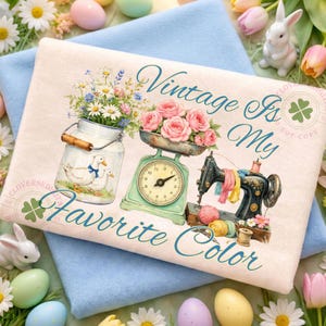 May include: A cream-colored decorative pillow with the text "Vintage Is My Favorite Color." The design features a vintage scale with pink roses, a sewing machine, and a jar with daisies and ducks.