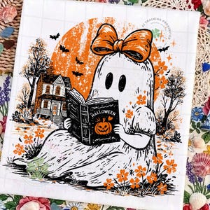 Op de afbeelding: Een vierkante print met een witte geest die een grote oranje strik draagt, zittend in een veld met oranje bloemen en een boek leest met de titel Halloween. De achtergrond bevat een grote oranje maan, een huis en vliegende vleermuizen in zwarte en oranje inkt.