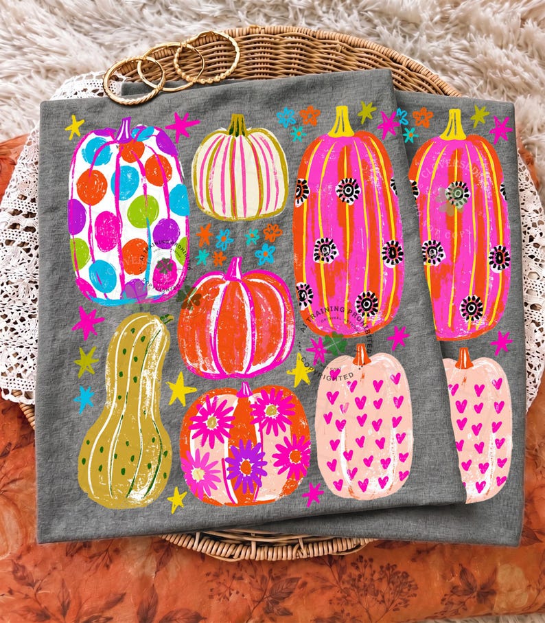 May include: A grey fabric item featuring a colourful graphic print of various pumpkins. The pumpkins are decorated with patterns including polka dots, stripes, flowers, and hearts in bright shades of pink, orange, blue, and yellow, accented by stars.