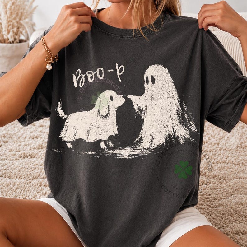May include: A charcoal gray short-sleeve t-shirt featuring a white graphic print of a small dog wearing a ghost costume facing a ghost. The text "Boo-p" is printed in white above the dog. The shirt has a crew neckline and a relaxed fit.