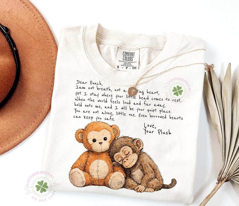 May include: Cream-colored Comfort Colors t-shirt featuring a graphic of two plush monkeys, one brown and one tan, with the text "Dear Punch, I am not breath..." and "Love, Your Plush". A gold necklace is draped across the shirt.