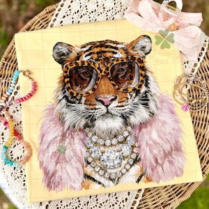 May include: A yellow canvas print featuring a tiger wearing leopard print sunglasses, a pink feather boa, and a diamond necklace. The tiger's fur is orange and black. A pink bow and jewelry are in the background.