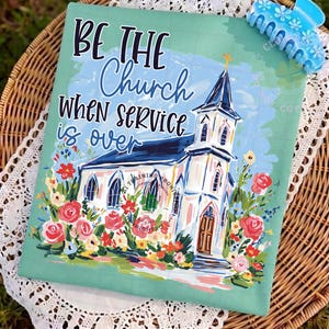 May include: A teal-colored decorative pillow with the text "BE THE Church WHEN SERVICE is over" and a painting of a white church with a blue roof and a gold cross. The church is surrounded by colorful flowers. A blue hair clip is in the upper right corner.