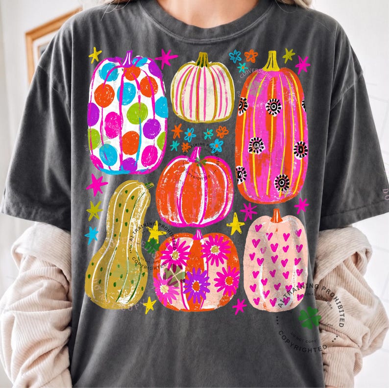 May include: A charcoal grey t-shirt featuring a graphic print of six colourful pumpkins in various patterns, including polka dots, stripes, flowers, and hearts, interspersed with small bright stars and flower shapes in neon colours.