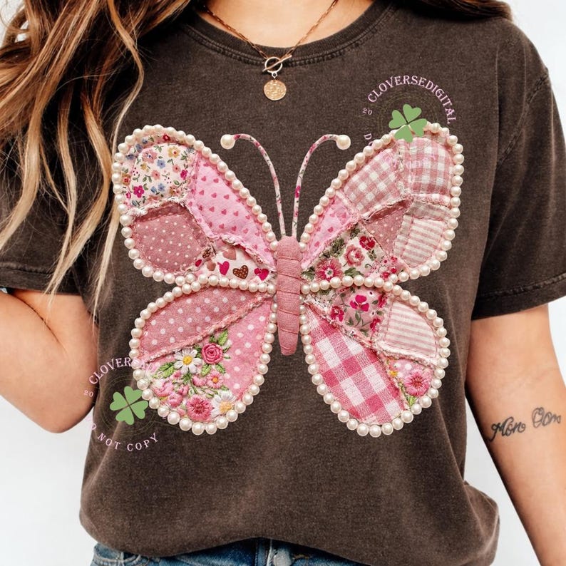 May include: Dark brown t-shirt featuring a large, patchwork butterfly design. The butterfly has pink wings with various patterns, including polka dots, floral prints, and gingham. The design is outlined with faux pearls. Text on the shirt reads "CLOVERSEDIGITAL" and "NOT COPY".
