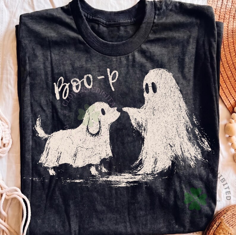 May include: A charcoal gray crew neck t-shirt featuring a white distressed graphic of a dog and a ghost standing together. Above the figures, the text reads "BOO-p" in a white script font. The design has a textured, weathered appearance.