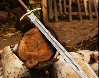 May include: A detailed image of a long sword with a patterned blade and a gold-colored crossguard. The handle is wrapped in a dark brown material. The sword rests on a pile of cut logs, with a blurred background of wooden structures.