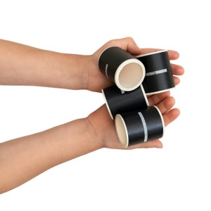 May include: A set of four black and white patterned paper tubes. The tubes are held in a person's hands.