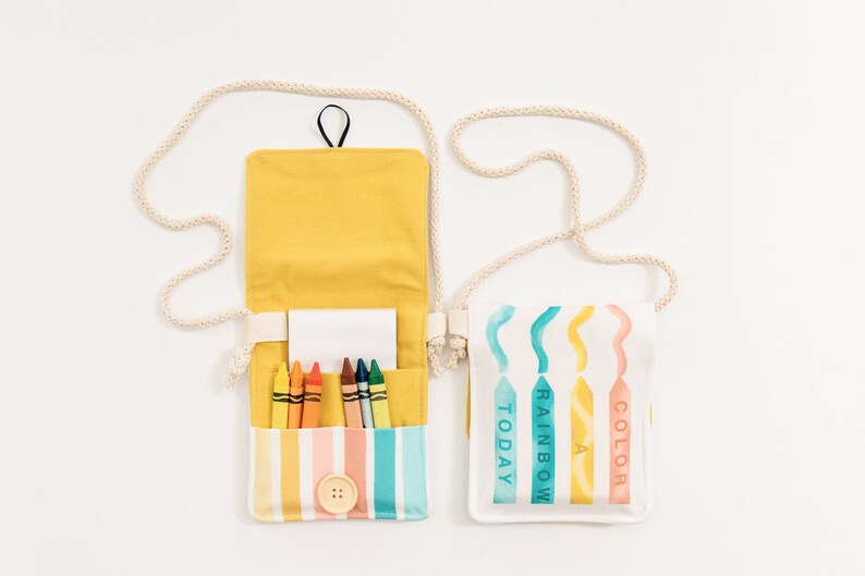 May include: Two small canvas bags with adjustable straps. One bag is yellow with a white stripe and rainbow colored crayons inside. The other bag is white with a rainbow design and the words "Color Today Rainbow" printed on it.