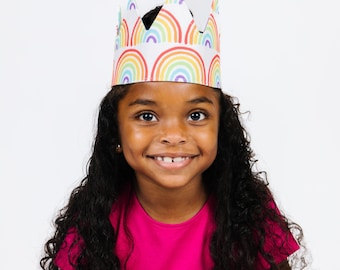 May include: A paper crown featuring a repeating pattern of colorful rainbows in shades of red, orange, yellow, green, blue, and purple. The crown has a pointed top edge and is constructed from white paper with a smooth, matte finish.