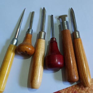 Puede incluir: Conjunto de seis herramientas con mango de madera y punta metálica. Los mangos son de varios tonos de amarillo, marrón y rojo. Las herramientas tienen diferentes formas de punta, para trabajos de detalle.