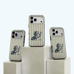 Könnte beinhalten: Drei Handyhüllen mit einem vertikal gestreiften Muster in Beige und Weiß. Jede Hülle zeigt eine Schwarz-Weiß-Illustration eines Dackelhundes, der ein Martiniglas hält. Die Hüllen werden auf weißen geometrischen Blöcken präsentiert.