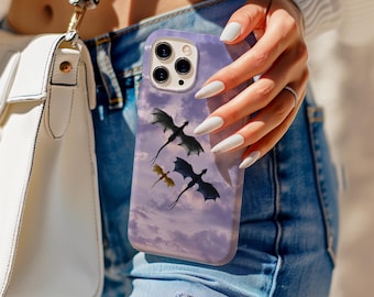 Op de afbeelding: Een lila telefoonhoesje met een ontwerp van drie draken die tegen een bewolkte lucht vliegen. De hoes heeft een glanzende afwerking en een uitsparing voor de camera. De telefoonhoes wordt vastgehouden door een persoon die een blauwe spijkerbroek en een witte handtas draagt.