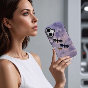 May include: A purple phone case featuring a cloudy sky design with three dragon silhouettes in black, gray, and yellow. The case has a glossy finish and is designed for a smartphone.