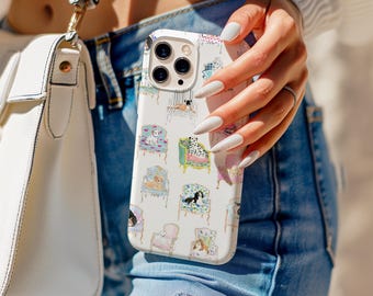 Puede incluir: Una funda de teléfono blanca con un patrón repetido de ilustraciones de perros en sillas ornamentadas. La funda se sostiene frente a una persona que lleva vaqueros azules y un suéter blanco. Un bolso blanco es visible en el fondo.