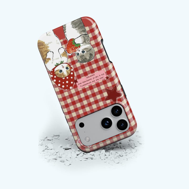 May include: A phone case with a red and white gingham pattern. The case features illustrations of cats with strawberries. One cat wears a strawberry costume. Text on the case reads, "Just like the strawberry, life is full of sweetness and surprises."