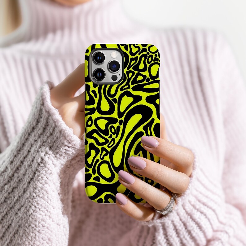 K&ouml;nnte beinhalten: Eine Handyh&uuml;lle mit einem neon-gelben und schwarzen Muster. Das Case hat ein sich wiederholendes abstraktes Design aus schwarzen organischen Formen auf einem leuchtend gelben Hintergrund. Die Handyh&uuml;lle wird von einer Person gehalten.
