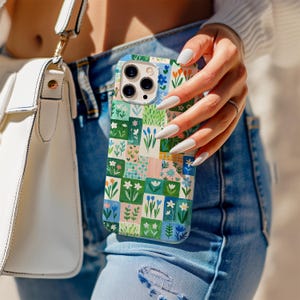 Könnte beinhalten: Eine bunte Handyhülle mit einem floralen Patchwork-Design. Die Hülle zeigt eine Vielzahl von Blumen und Grün in einem Rastermuster. Eine weiße Handtasche und blaue Jeans sind im Hintergrund.