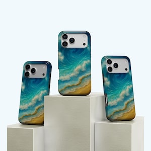 Może przedstawiać: Trzy etui na telefon z motywem plażowym. Etui przedstawiają żywe przedstawienie fal oceanu w odcieniach niebieskiego i turkusowego, rozbijających się o piaszczysty brzeg. Etui są wyświetlane na białych geometrycznych blokach.