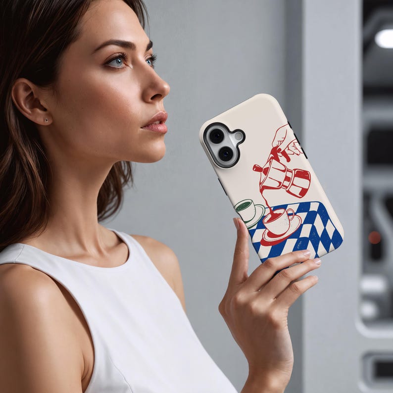 May include: A cream phone case with a red and white coffee pot illustration pouring into a cup, set against a blue and white chequered tablecloth. The case has a black border and a camera cutout.