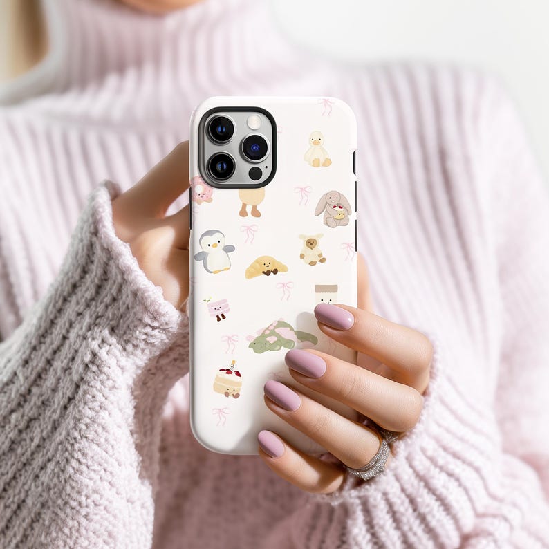 May include: A white phone case featuring a repeating pattern of cute cartoon animals and pink bows. The case has a camera cutout and is held in a person's hands. The animals include a penguin, duck, bunny, and bear.