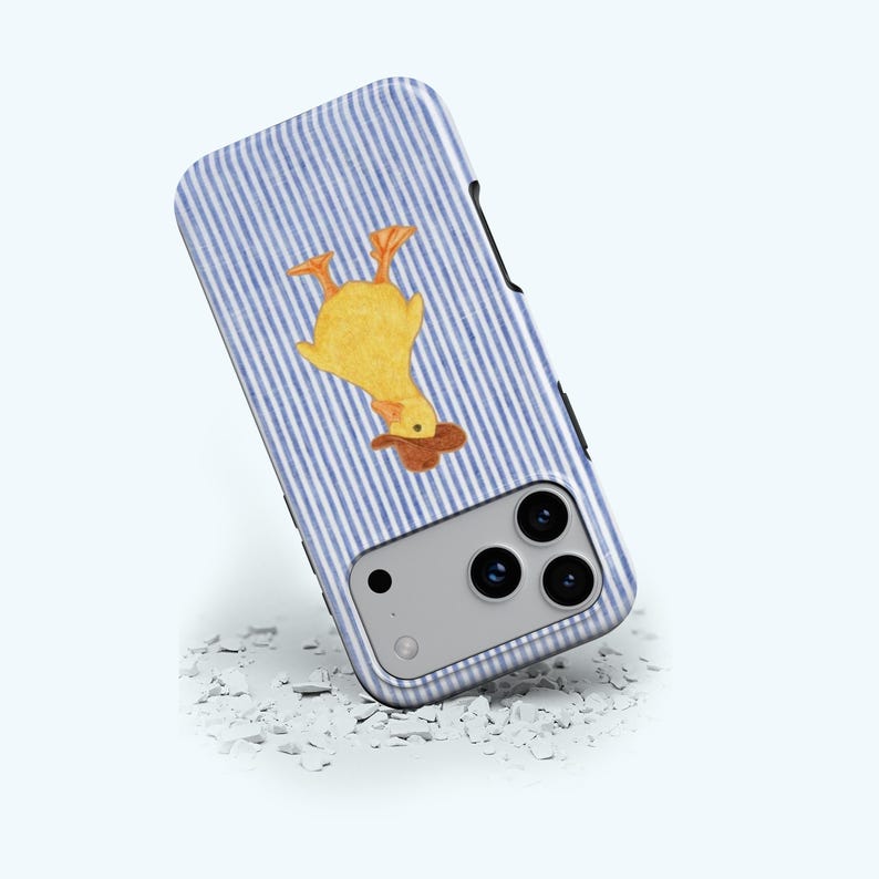 May include: A smartphone case featuring a yellow duck illustration on a blue and white striped background. The case has a camera module with three lenses and a flash. The case is resting on a white, textured surface.