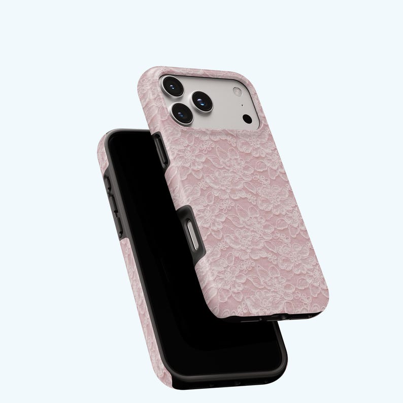 May include: A pink phone case with a white lace pattern. The case is shown with a black phone inside, and the case is slightly angled to show the design. The case has a black border and a raised edge around the camera.