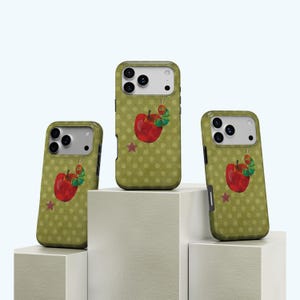 May include: Three olive green phone cases with a red apple and caterpillar design. The cases have a polka dot pattern and a red star. The cases are displayed on white blocks.