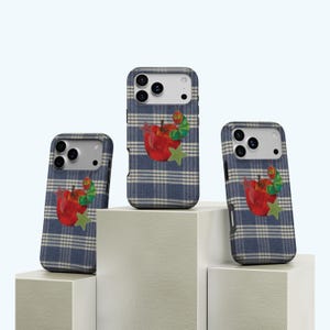 May include: Three phone cases with a blue and white check pattern. Each case features a red apple with a green caterpillar and a green star. The cases are displayed on white geometric blocks.