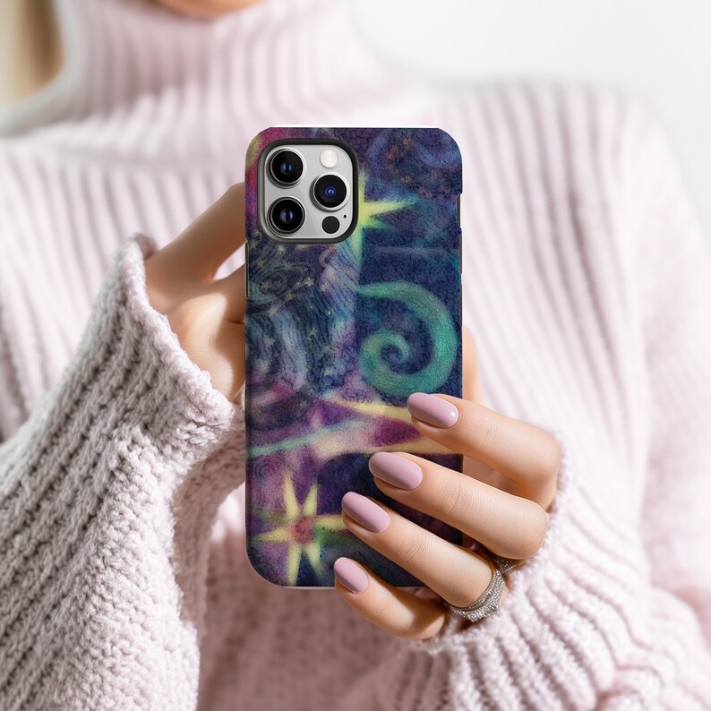 May include: A smartphone case with a colorful abstract design. The case features a swirling pattern of blues, purples, and greens, with yellow accents. The case is held in a person's hands, with a pink sweater in the background.