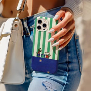 Op de afbeelding: Een telefoonhoesje met een groen en wit gestreept patroon, met een blauwe basis en een cartoonillustratie van een krokodil en een muis. De hoes wordt vastgehouden door een persoon die een blauwe spijkerbroek draagt.