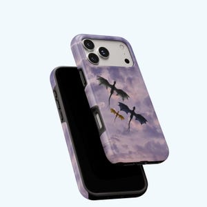 May include: A phone case featuring a fantasy scene with three dragons soaring through a cloudy, purple sky. The case is a light purple color with a black border and a glossy finish. The design is a digital illustration.
