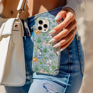 May include: A light blue phone case featuring a pattern of various cats among green foliage and flowers. The case has a camera cutout and is held by a person wearing blue jeans and a white purse.