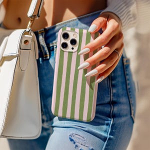 Könnte beinhalten: Smartphone-Hülle mit vertikalem Streifenmuster in Olivgrün und Hellrosa. Die Hülle wird in einer Hand gehalten, mit einer weißen Handtasche und Jeans im Hintergrund.