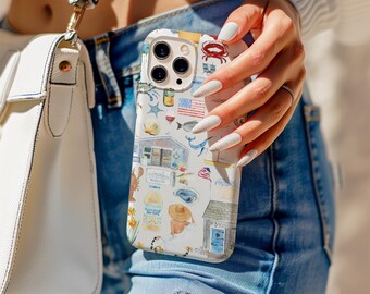 Puede incluir: Una funda blanca para iPhone con un diseño costero colorido que presenta una langosta, una cabaña de playa, la bandera estadounidense y otros elementos náuticos. La funda la sostiene una persona que lleva vaqueros azules y un suéter blanco, con un bolso blanco en el fondo.