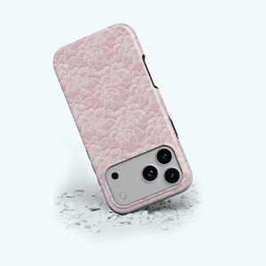 May include: A pink phone case with a floral pattern. The case has a textured surface and a black border. The phone case has three camera lenses and a flash.