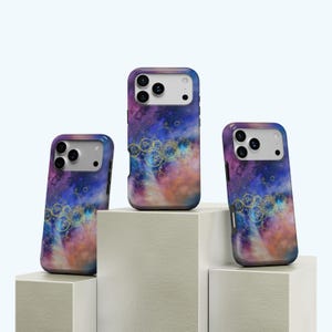 Op de afbeelding: Drie telefoonhoesjes met een kleurrijk, abstract ontwerp. De hoesjes tonen een mix van paarse, blauwe en oranje tinten, versierd met gouden cirkelvormige patronen. Ze worden gepresenteerd op witte geometrische blokken, die hun ontwerp benadrukken.