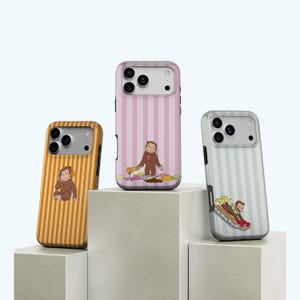 May include: Three phone cases featuring cartoon monkey illustrations. One case has an orange and white striped design with a monkey wearing headphones. Another has a pink and white striped pattern with a monkey pouring paint. The third has a blue and white striped pattern with a monkey sledding.