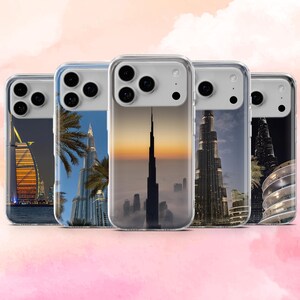 Peut inclure: Plusieurs coques de téléphone transparentes avec des monuments de Dubaï. Les coques présentent des images du Burj Khalifa, du Burj Al Arab et des paysages urbains, sur fond rose.