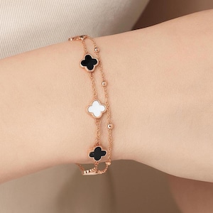 May include: Rose gold bracelet featuring a clover design with black and white enamel. The bracelet has a delicate chain with small, round beads. The clover charms are evenly spaced along the chain.