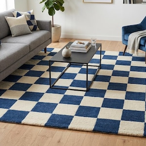 Könnte beinhalten: Ein großer rechteckiger Teppich mit einem sich wiederholenden Schachbrettmuster in tiefem Marineblau und Off-White. Der Teppich hat eine strukturierte, getuftete Oberfläche und bedeckt einen großen Teil des hellen Holzbodens im Raum.