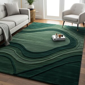 Könnte beinhalten: Ein grüner Teppich mit einem wellenförmigen Design. Der Teppich hat verschiedene Grüntöne, die einen strukturierten, geschichteten Effekt erzeugen. Der Teppich liegt auf einem Holzboden in einem Wohnzimmer. Die Maße des Teppichs sind in Zentimetern.