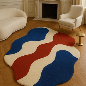 Könnte beinhalten: Ein moderner, abstrakter Teppich mit einem wellenförmigen Design in Blau, Rot und Creme. Die einzigartige Form und Farbgebung des Teppichs verleihen jedem Wohnraum eine moderne Note. Der Teppich ist ca. 152 cm breit und 203 cm lang.
