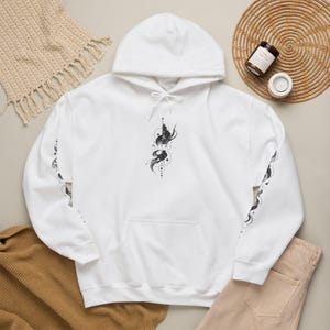 May include: A white hooded sweatshirt featuring a black graphic design on the center chest and down both sleeves. The central graphic includes abstract swirling lines, geometric circles, and the text NITKI STUDIO in a small, clean font.